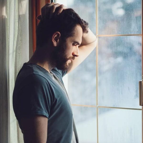 A man standing beside a window with signs of mental distress